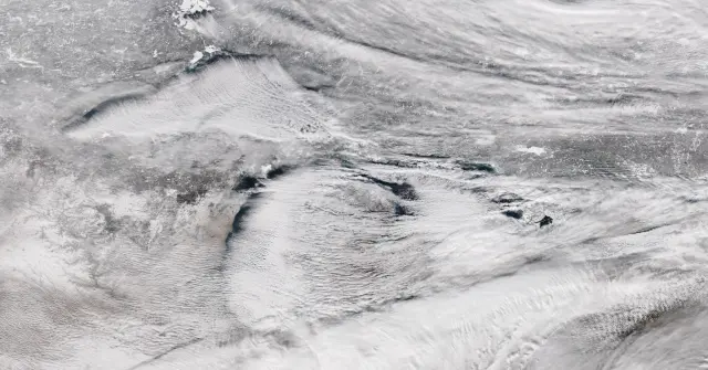 Satellite view of bands of lake-effect snow clouds streaming eastward off the Great Lakes over snow-covered ground.